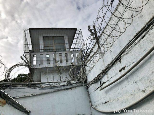 厳重に鉄条網が張られた監獄の壁と監視塔